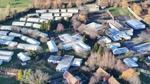 Eddie Mitchell Drone shot of dozens of buildings around one larger building at the Northeye site. All have white roofs and trees can be seen among the buildings. 