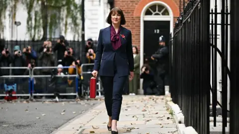 Getty Images Rachel Reeves carries the red Budget Box as she leaves 11 Downing Street. A crowd of journalists and camera operators are in the background, standing behind a fence.