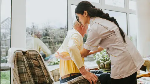 Getty Images A care worker helps lift an elderly man from an armchair