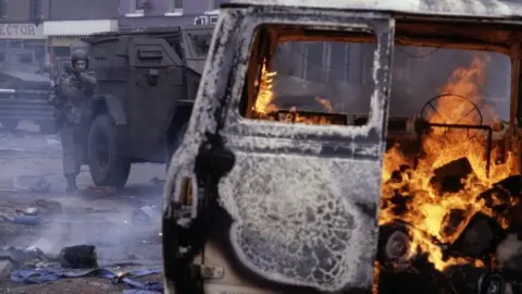 Getty Images Car on fire with army personnel behind it during the Troubles