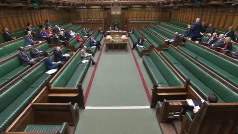 A picture of the debate on Jim Allister's bill in the House of Commons. The seats are green and brown wood benches and many of the seats are empty.