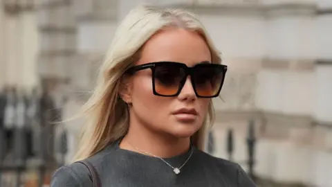 PA Media Victoria Thomas Bowen arriving at court. She has long blonde hair and is wearing black sunglasses, a silver necklace and a grey dress.