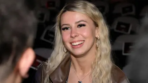 Getty Images Haliey Welch shown in a close up photograph at an event in November, wearing a brown leather jacket and smiling.