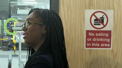 BBC Kemi Badenoch stands by a door with a sign reading: 