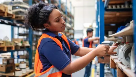 Getty Images Woman wearing a hi-vis jacket scanning items in a warehouse