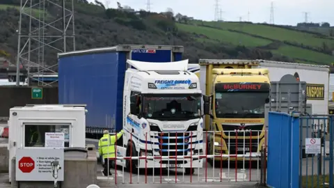 Getty Images A man dressed in a high-visibility jacket has his hand reached to gather documents from a truck driver.