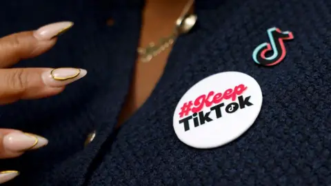 Getty Images A woman with long nails wears a badge reading 