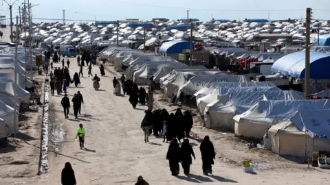 Reuters A group of women walks down a path between dozens of tents.