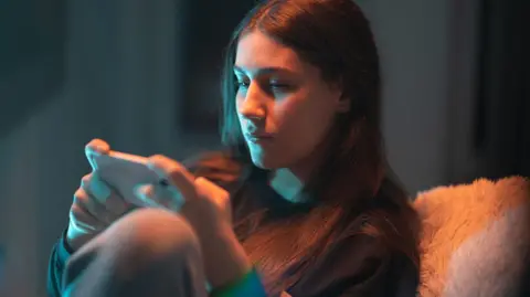 Getty Images A young woman plays a mobile game on her phone in a dimly-lit room