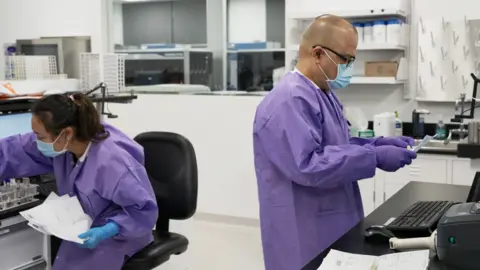 Karius Lab workers in purple lab coats examine tests