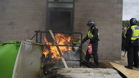 PA Media A fire is extinguished by police officers as trouble flares outside the Holiday Inn Express in Rotherham, South Yorkshire