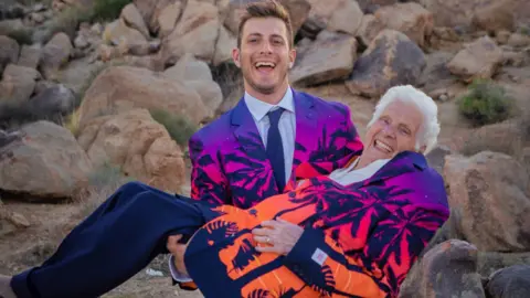 Ross Smith Young man in colourful blazer holds an older woman in the same blazer