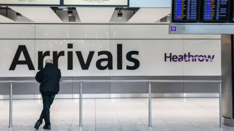 Getty Images Man waiting in front of a large 'Arrivals' sign at Heathrow airport