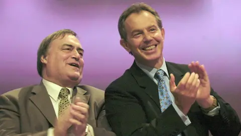 BBC News John Prescott pictured with Tony Blair pictured together. Both men are clapping.