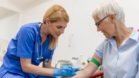 Getty Images A doctor performs a blood test on a smiling patient