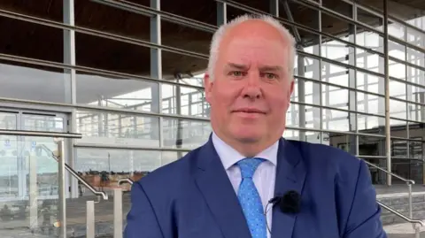 BBC Andrew RT Davies stood in front of the Senedd wearing a dark blue suit and a light blue tie.