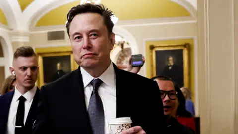 Reuters Elon Musk walks through Capitol Hill holding a takeaway coffe in his hand and looking away from camera, wearing a suit and tie and followed by security officers and journalists, in Washington DC on 5 December.