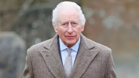 Getty Images King Charles III attends the Sunday service at the Church of St Mary the Virgin, close to the Sandringham Estate. The King is wearing a brown tweed coat, navy suit and a lightly decorated tie. He is looking towards the camera lens from a distance