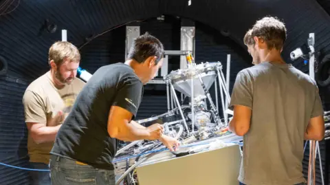 Sierra Space Three Sierra Space engineers work on a machine designed to produce oxygen from a substitute for moon dust