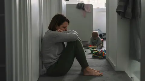 Getty Images Generic picture of a mother sitting on the floor with her baby in the background