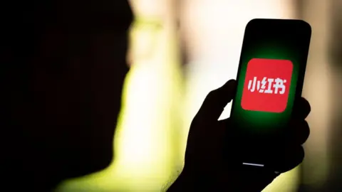 Getty Images Backview of a man holding a phone, with the Xiaohongshu logo displayed on the phone.

