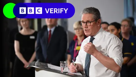 PA Media Prime Minister Sir Keir Starmer speaks to an audience. He is wearing a white shirt and a glass of water sits on the lectern in front of him. 