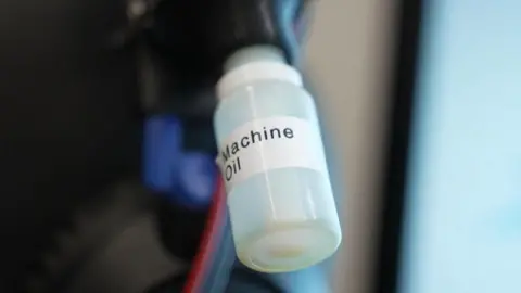 A clear plastic bottles attached to a machine with a label on it reading 