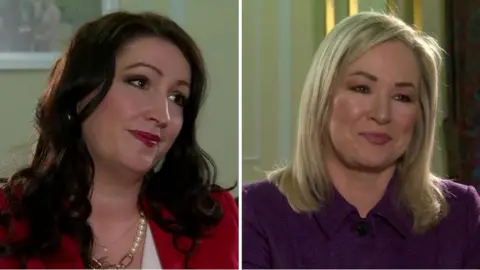 Emma Little-Pengelly and Michelle O'Neill being interviewed by BBC News NI.  Emma has long, dark curly hair and is wearing a red jacket and a white blouse.   Michelle has shoulder-length straight blonde hair and is wearing a purple tweed suit. 