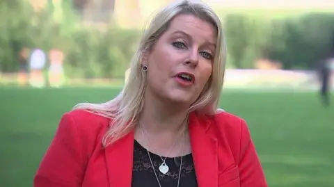 Mims Davies being interviewed on College Green in Westminster, wearing a red jacket. 