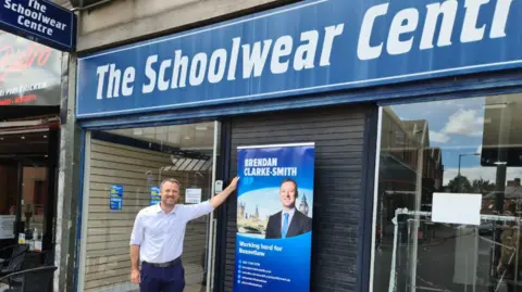 Brendan Clarke-Smith standing outside the Schoolwear Centre, which later became his office