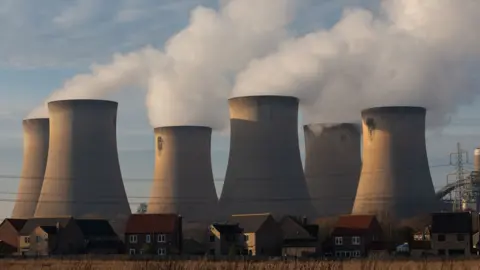 Getty Images Draw power station. The photo shows smoke billowing out of six stout chimneys. There are a row of houses and a number of electricity cables in the foreground.