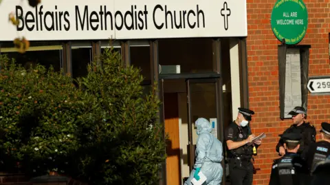 Reuters Forensics and police outside the church. One forensic worker is walking inside the church and two police officers are taking notes while standing outside