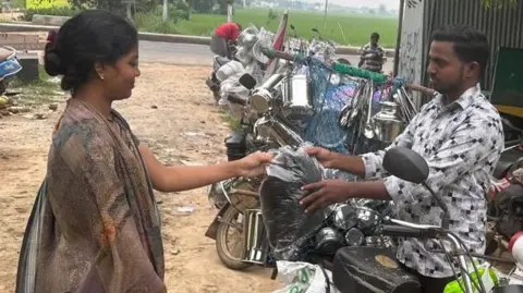 Kolachi Venkatesh A lady hands a bag of hair to Kolachi Venkatesh who is standing next to his scooter.