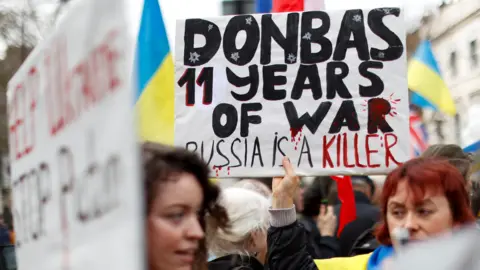 Reuters Two women stand in a crowd of protesters, one holding up a poster saying 