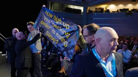 PA Media Protesters hold up a banner reading 'How high up your 