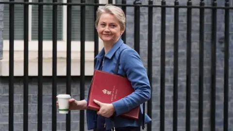 PA Media Home Secretary Yvette Cooper walking along Downing Street holding a red folder and coffee cup