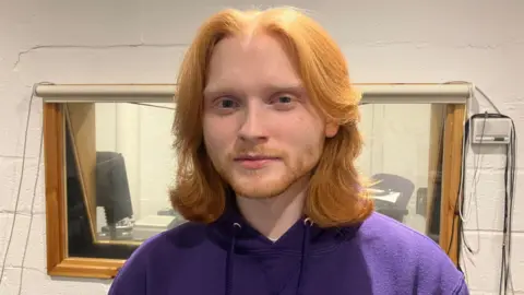 BBC / Kate McGough Harry looks into the camera in a head and shoulders image. He is wearing a purple hoodie and has long ginger hair down to his shoulders, and a cropped ginger beard.