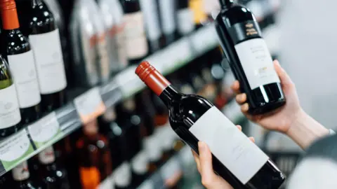 Getty Images A person comparing two bottle of wine in a supermarket