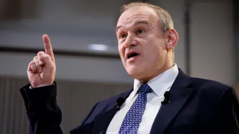 PA Media Liberal Democrats Party leader Sir Ed Davey points to the sky as he delivers a speech regarding British leadership on trade and defence.