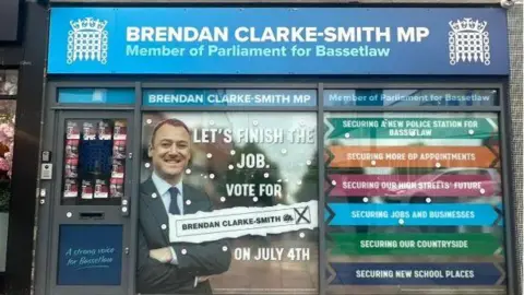 BBC Ex-MP Brendan Clarke-Smith still has his office displaying his title as MP, with the portcullis logo of the House of Commons and recent posters attacking the Labour government's winter fuel allowance cuts in the window.