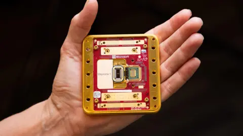 Microsoft A photograph of the new Majorana 1 chip which is a gold and red square, held in the palm of an open hand (Microsoft press image)