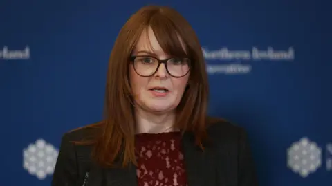 PA Media Caoimhe Archibald wearing a dark coloured suit with a blue background behind her. 