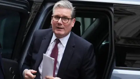 PA Media Sir Keir Starmer leaves from a vehicle with a piece of paper in his left hand. He has a neutral expression on his face.