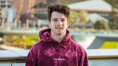 Samuel Weidenhofer Samuel Weidenhofer wearing a deep red hoodie.