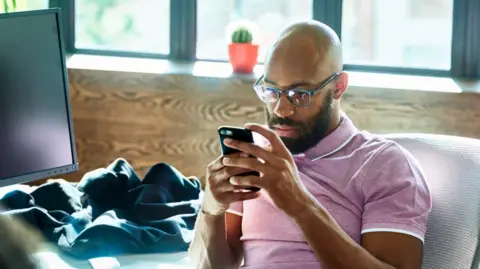 Getty Images A man in a pink shirt looks at his phone at work