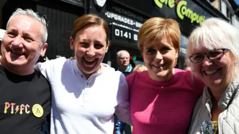 Getty Images From left to right - Alan Black with silver hair and a black shirt reading PT FC, Mhairi Black in a white top, Nicola  Sturgeon in a pink top and Mhairi Black's mother, who has blond hair, a grey coat and an SNP pin badge  