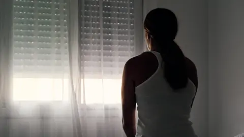 Getty Images Rear view of an unrecognisable woman sitting on her bed looking out of a window