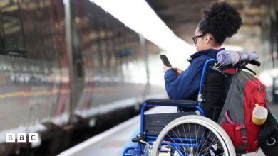 A woman in a wheelchair waiting to board a train, whilst using her phone.