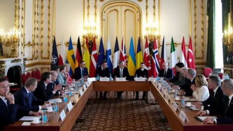 EPA The 18 world leaders gathered around a U-shaped table with their countries' flags behind them in a room with white walls and gold detail. Sir Keir Starmer is sitting in the centre with Emmanuel Macron and Volodymyr Zelensky flanking him.