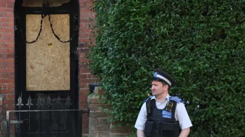 Reuters A police officer stands outside a house with a boarded-up door